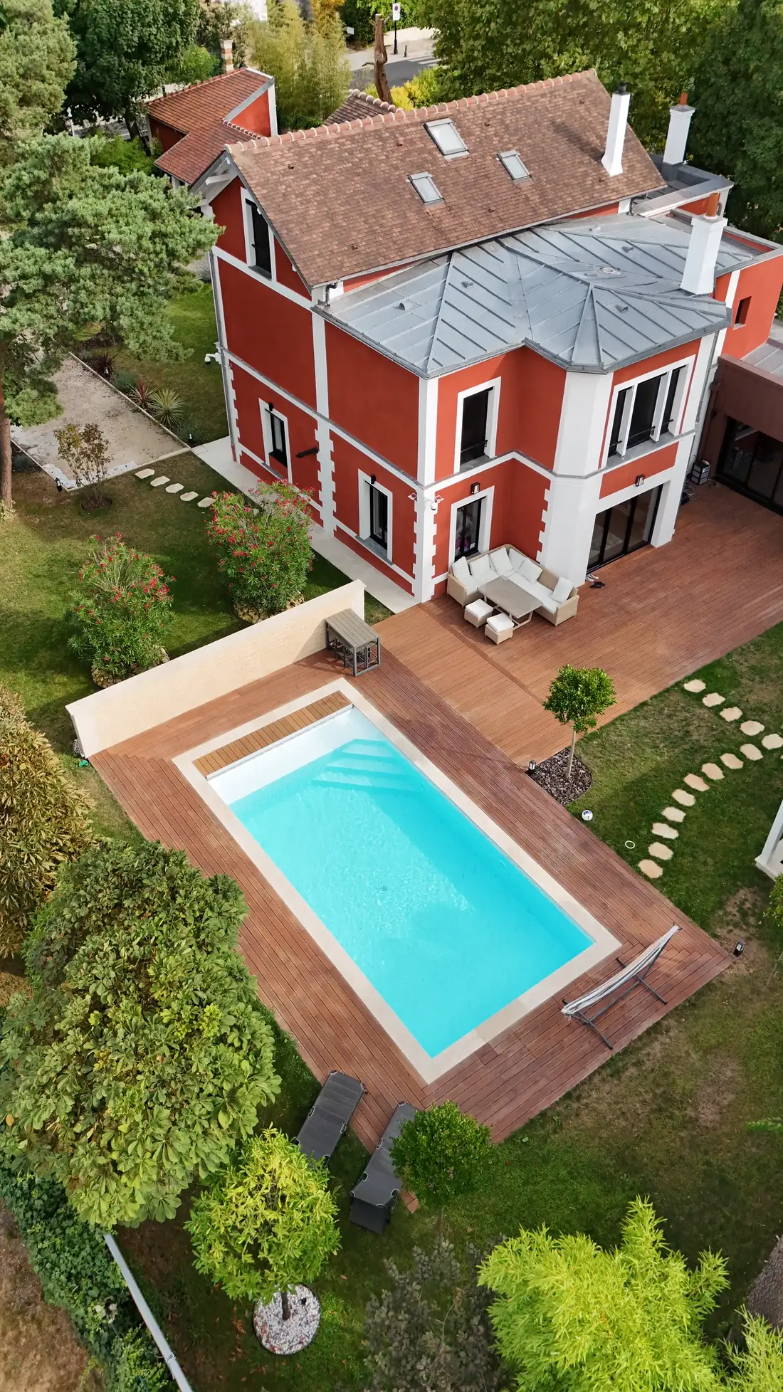 Piscine rectangulaire bordée d'une terrasse en bois exotique, devant une maison de maître